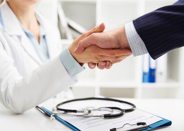 A doctor in a white coat shakes hands with someone in a business suit.